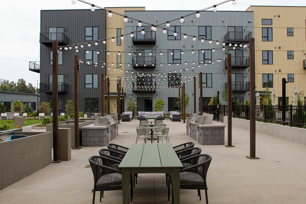 Outdoor communal seating area with tables, chairs, string lights, and a modern apartment building backdrop